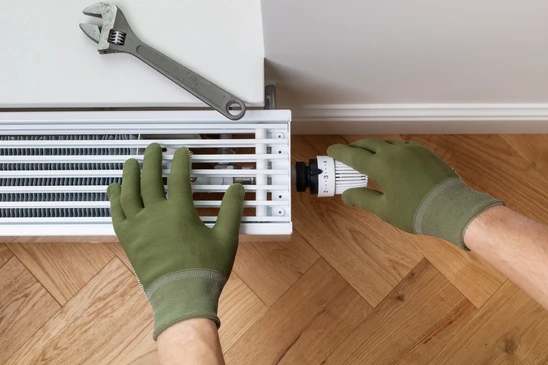 Intérieur technique, plombier ajuste un collecteur de chauffage au sol avec une clé